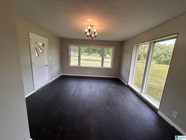 unfurnished dining area featuring baseboards, a textured ceiling, an inviting chandelier, and dark wood-style flooring