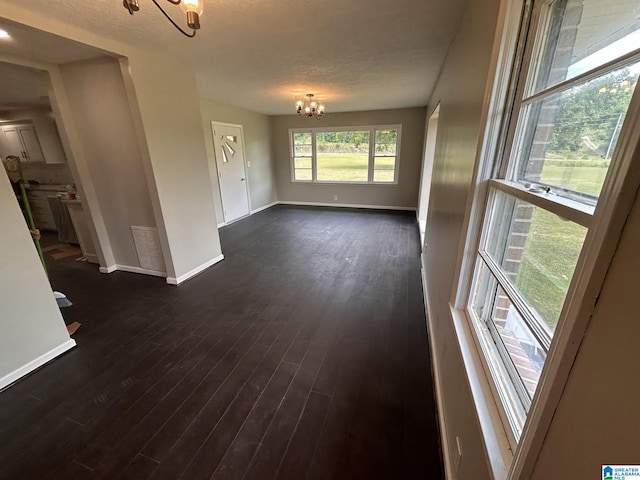 empty room featuring visible vents, a textured ceiling, dark wood-style floors, baseboards, and a chandelier