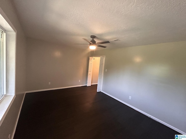 empty room with ceiling fan, baseboards, a textured ceiling, and dark wood-style floors