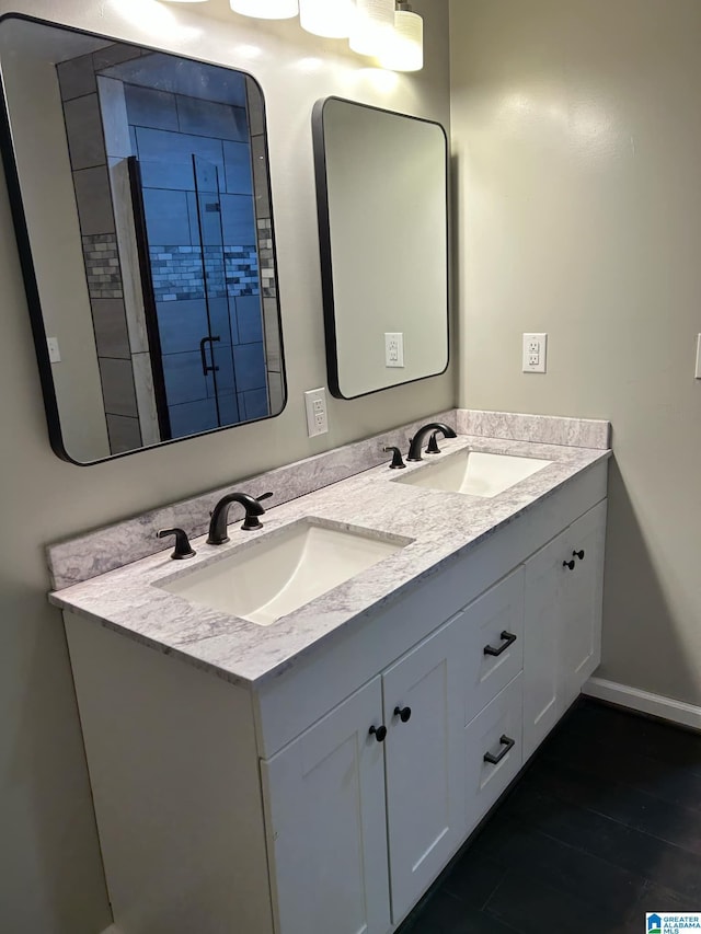 bathroom with double vanity, a shower stall, baseboards, and a sink