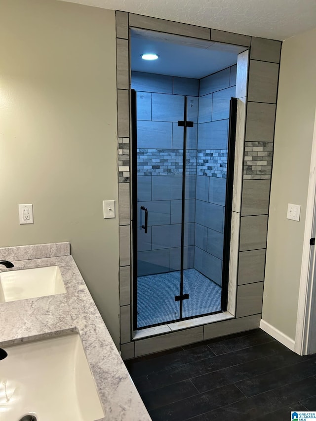 bathroom with baseboards, wood finished floors, a stall shower, and a sink