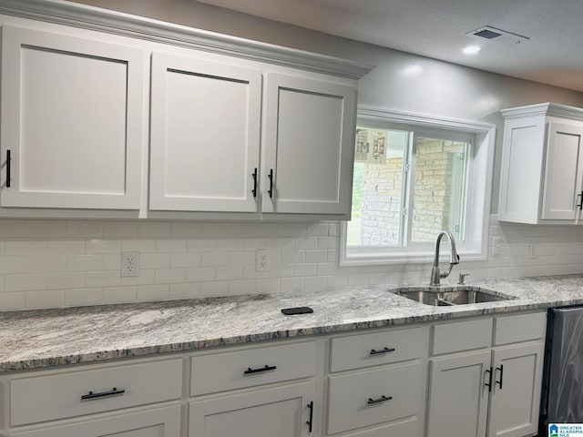 kitchen featuring tasteful backsplash, visible vents, dishwashing machine, white cabinets, and a sink