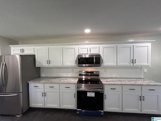 kitchen featuring tasteful backsplash, white cabinets, appliances with stainless steel finishes, and light stone countertops