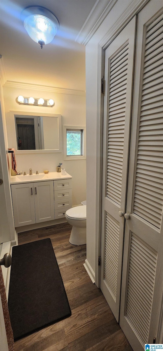 bathroom with wood-type flooring, ornamental molding, vanity, and toilet