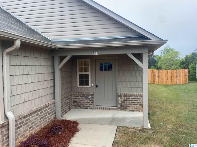 property entrance featuring roof with shingles, a yard, fence, and brick siding