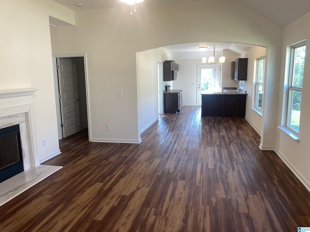 unfurnished living room featuring a chandelier, dark wood-style flooring, a fireplace, baseboards, and vaulted ceiling