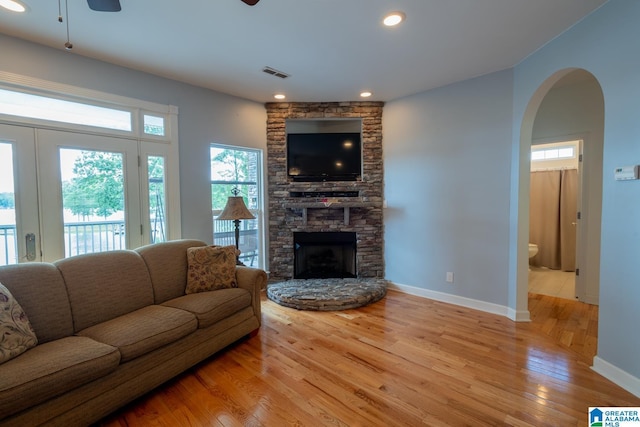 living room featuring ceiling fan, a stone fireplace, and light hardwood / wood-style floors