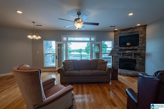 living room featuring ceiling fan with notable chandelier, a fireplace, and light hardwood / wood-style flooring