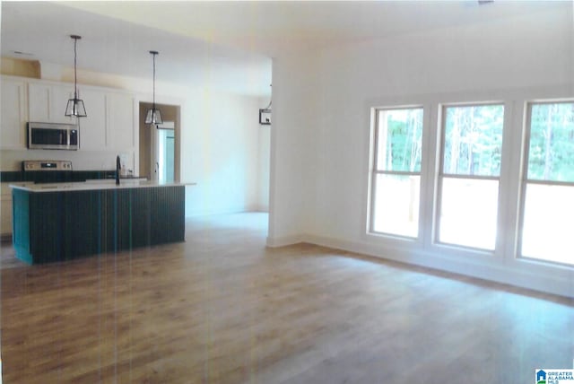 kitchen with wood-type flooring, a center island with sink, white cabinets, pendant lighting, and appliances with stainless steel finishes