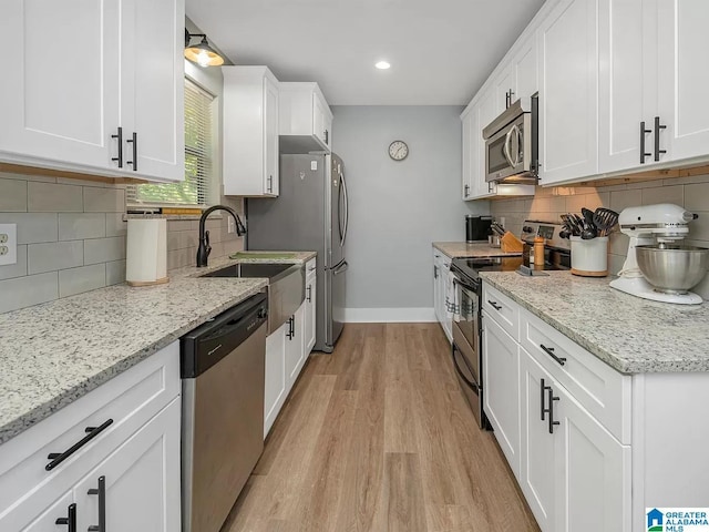kitchen with light wood-style flooring, a sink, white cabinetry, stainless steel appliances, and baseboards