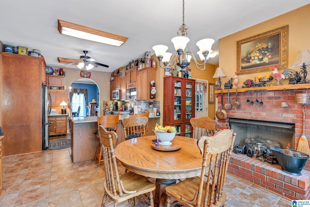 dining room with a brick fireplace and ceiling fan with notable chandelier