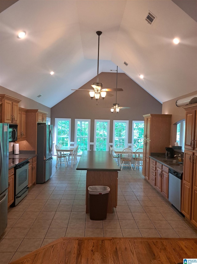 kitchen featuring appliances with stainless steel finishes, high vaulted ceiling, dark countertops, a kitchen island, and light tile patterned floors