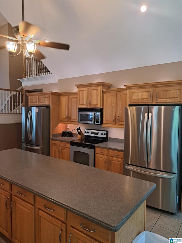kitchen with appliances with stainless steel finishes, dark countertops, a ceiling fan, light tile patterned floors, and brown cabinetry
