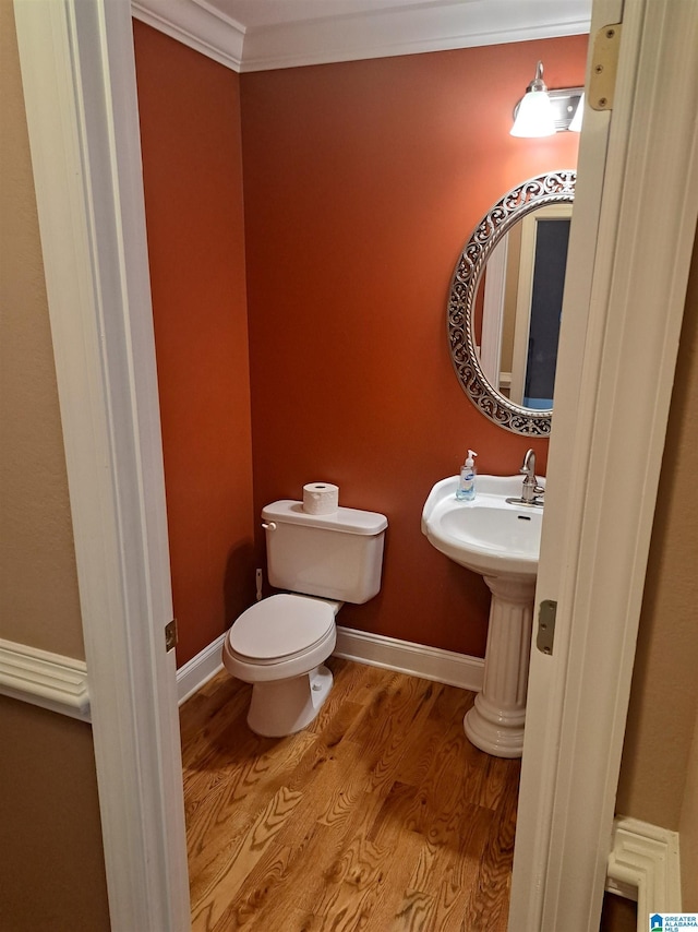 half bathroom with toilet, wood finished floors, and crown molding