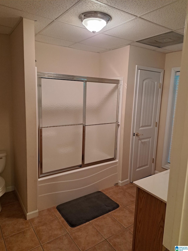 bathroom with tile patterned floors, toilet, a drop ceiling, baseboards, and enclosed tub / shower combo
