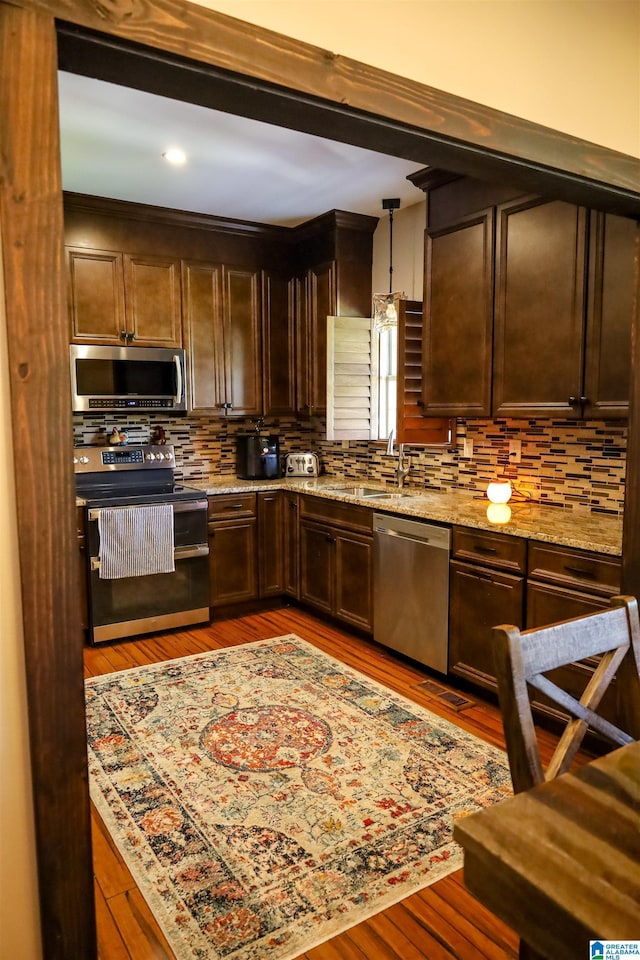 kitchen featuring sink, hanging light fixtures, light stone counters, light hardwood / wood-style floors, and appliances with stainless steel finishes