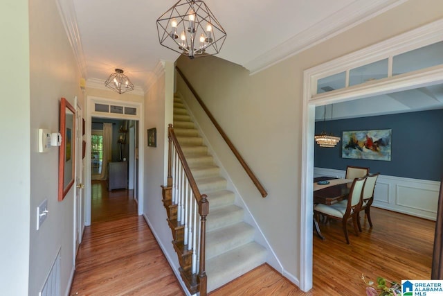 stairs featuring wood-type flooring, ornamental molding, and a notable chandelier