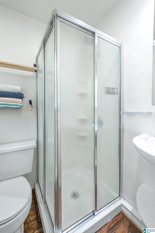 bathroom with a stall shower, toilet, and wood finished floors