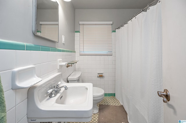 bathroom featuring a shower with curtain, a sink, toilet, tile walls, and a wainscoted wall
