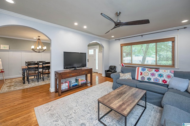 living room with arched walkways, ceiling fan with notable chandelier, crown molding, and wood finished floors