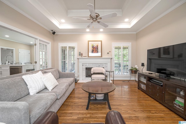 living room with a fireplace, ceiling fan, a tray ceiling, hardwood / wood-style floors, and ornamental molding