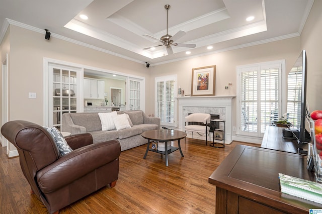 living room featuring ceiling fan, a tray ceiling, dark hardwood / wood-style flooring, and crown molding