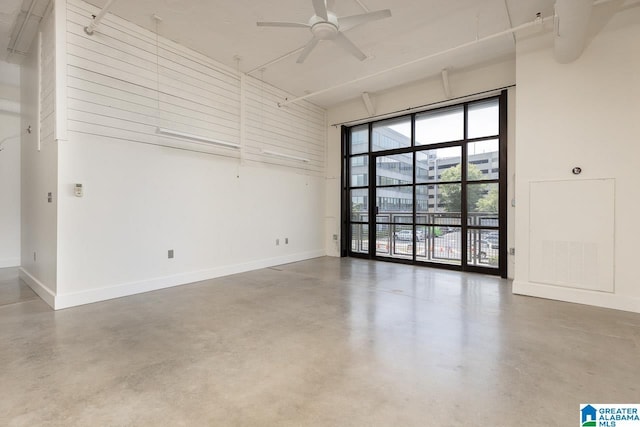 unfurnished room featuring concrete flooring, ceiling fan, and a high ceiling