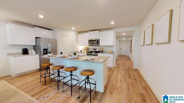 kitchen featuring a breakfast bar, a center island with sink, light hardwood / wood-style flooring, appliances with stainless steel finishes, and white cabinetry