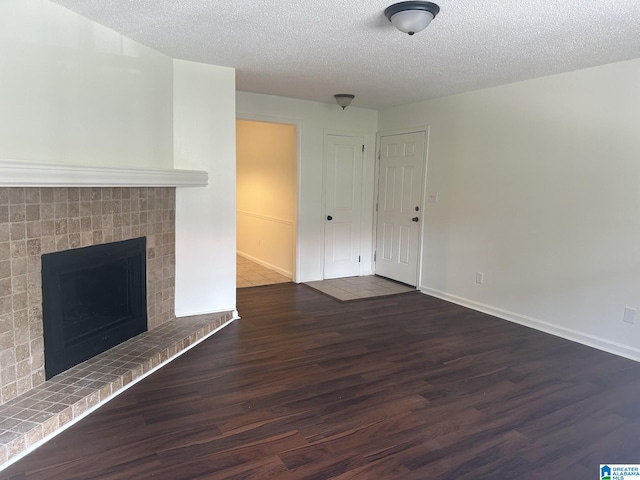 unfurnished living room featuring a brick fireplace, dark wood-type flooring, and a textured ceiling