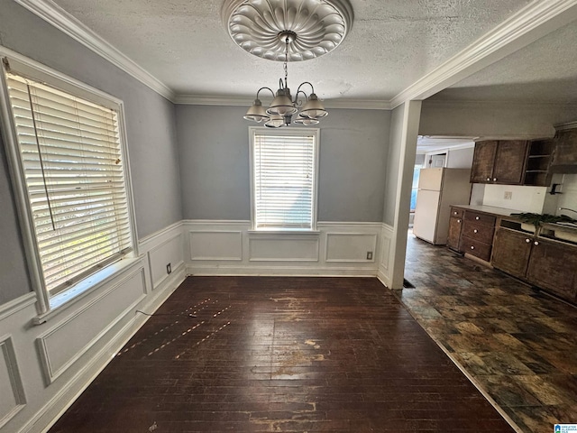 unfurnished dining area with crown molding, dark hardwood / wood-style floors, an inviting chandelier, and a textured ceiling