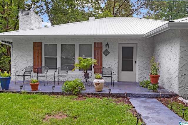 408 N Main St, Graysville, AL 35073 - view of exterior entry featuring stucco siding, a porch, metal roof, a chimney, and a yard