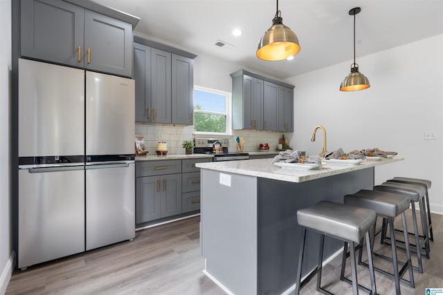 kitchen featuring light stone counters, hanging light fixtures, gray cabinets, backsplash, and appliances with stainless steel finishes