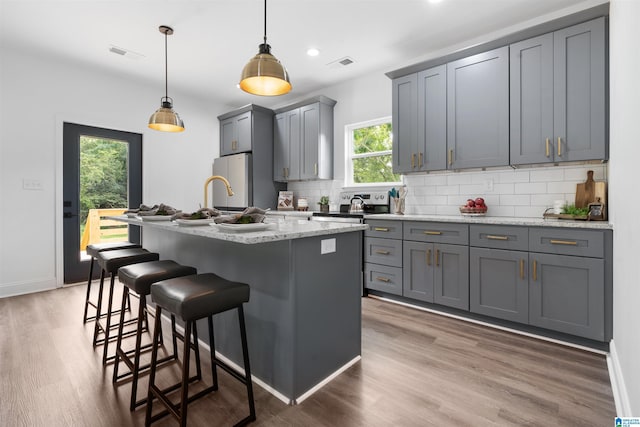 kitchen with gray cabinets, pendant lighting, backsplash, and a kitchen island with sink