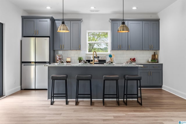 kitchen featuring stainless steel refrigerator, light stone countertops, gray cabinets, and a breakfast bar area