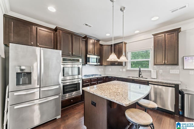 kitchen with light stone countertops, stainless steel appliances, sink, a center island, and hanging light fixtures