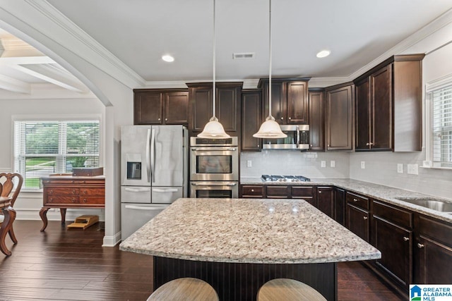 kitchen featuring a center island, stainless steel appliances, coffered ceiling, pendant lighting, and a kitchen bar