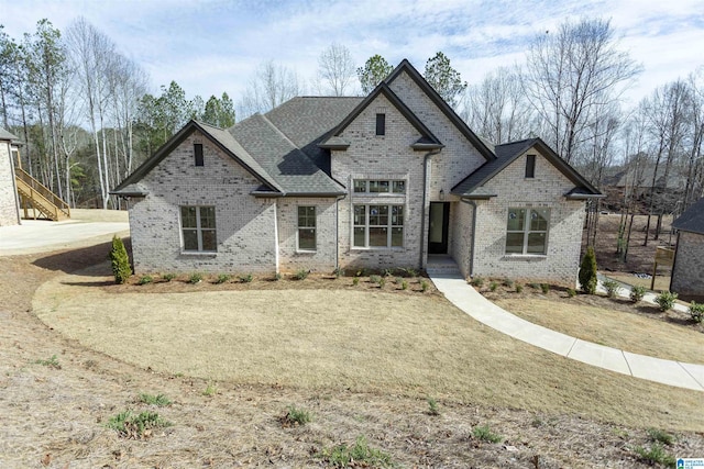 french provincial home with a shingled roof, a front lawn, and brick siding