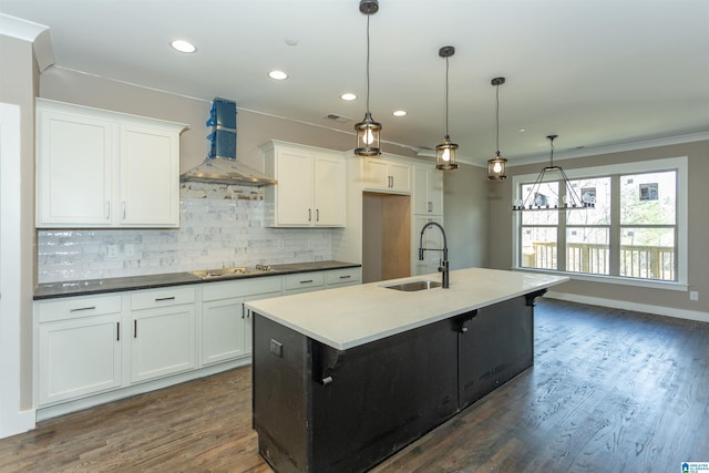 kitchen featuring electric cooktop, a sink, wall chimney range hood, an island with sink, and dark wood finished floors