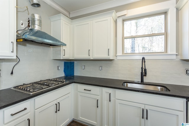 kitchen featuring wall chimney range hood, stainless steel gas stovetop, white cabinetry, and a sink