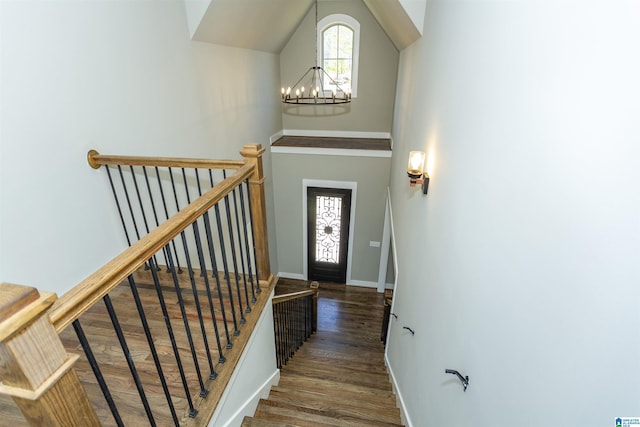 staircase featuring baseboards, a notable chandelier, a high ceiling, and wood finished floors