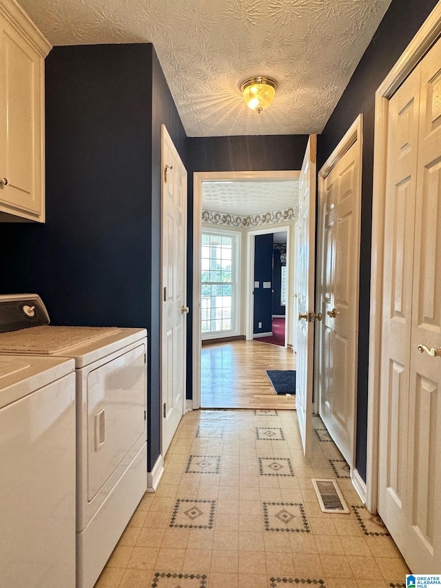 clothes washing area with washer and clothes dryer, cabinets, and a textured ceiling