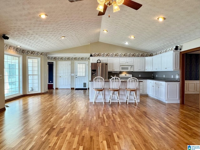 kitchen featuring white cabinetry, stainless steel refrigerator with ice dispenser, vaulted ceiling, a kitchen island with sink, and light wood-type flooring