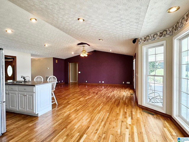 interior space with lofted ceiling, white cabinets, light wood-type flooring, a textured ceiling, and a breakfast bar area