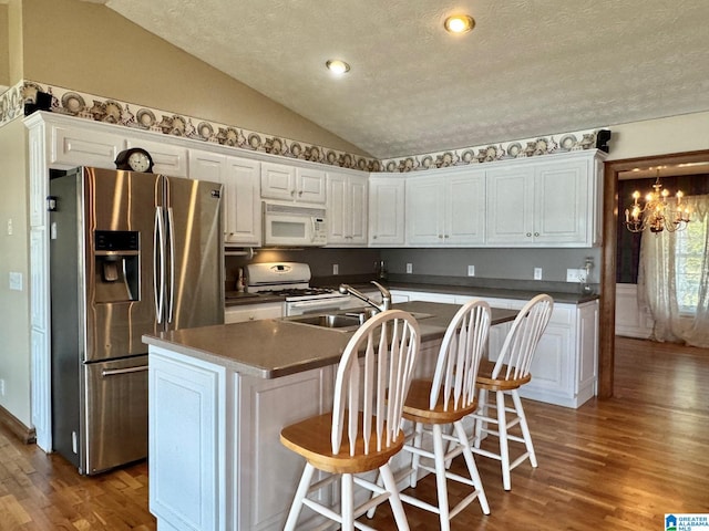 kitchen with white cabinets, lofted ceiling, white appliances, and an island with sink