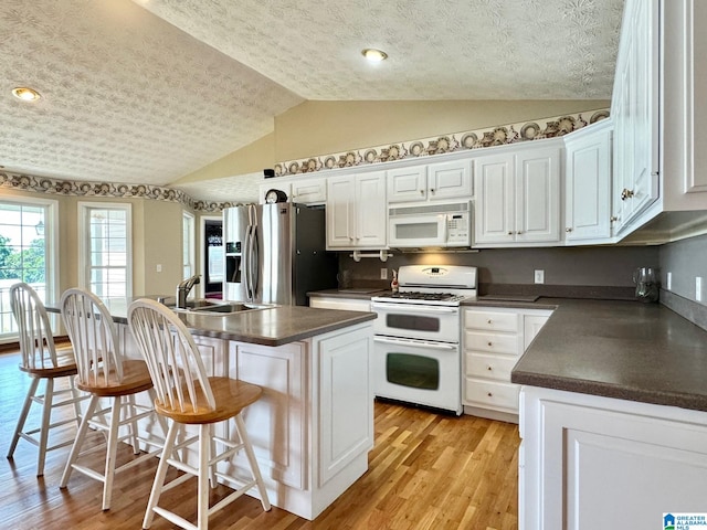 kitchen featuring a center island, white appliances, sink, vaulted ceiling, and white cabinetry