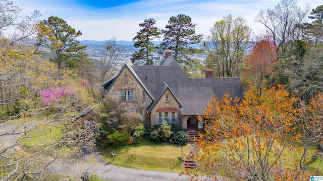 tudor home featuring a front yard, stone siding, a mountain view, and a chimney