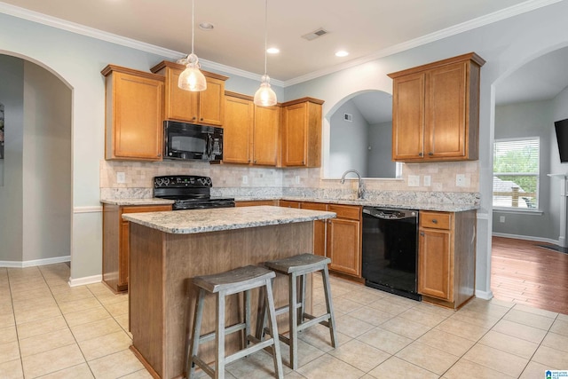 kitchen with light hardwood / wood-style flooring, black appliances, backsplash, and a center island