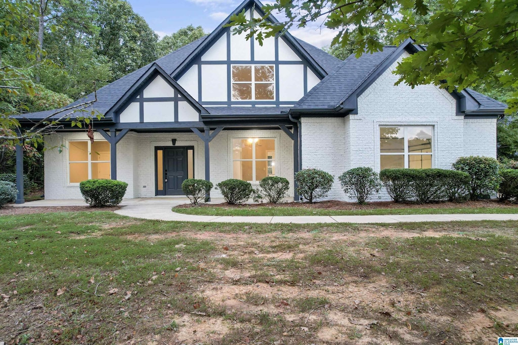 tudor home with covered porch and a front lawn