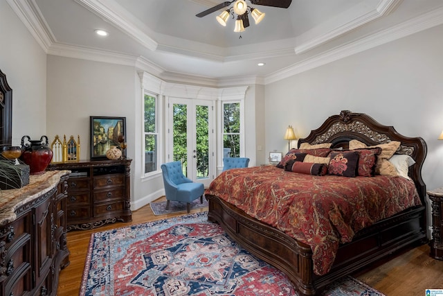 bedroom with crown molding, hardwood / wood-style flooring, a raised ceiling, and ceiling fan