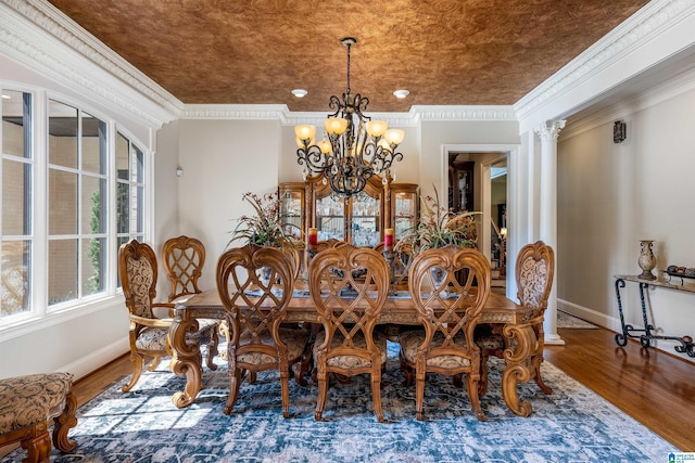 dining room featuring hardwood / wood-style flooring, crown molding, a chandelier, and ornate columns